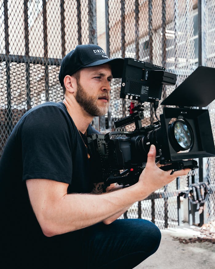 A male cinematographer operates a high-end camera outdoors, capturing footage.